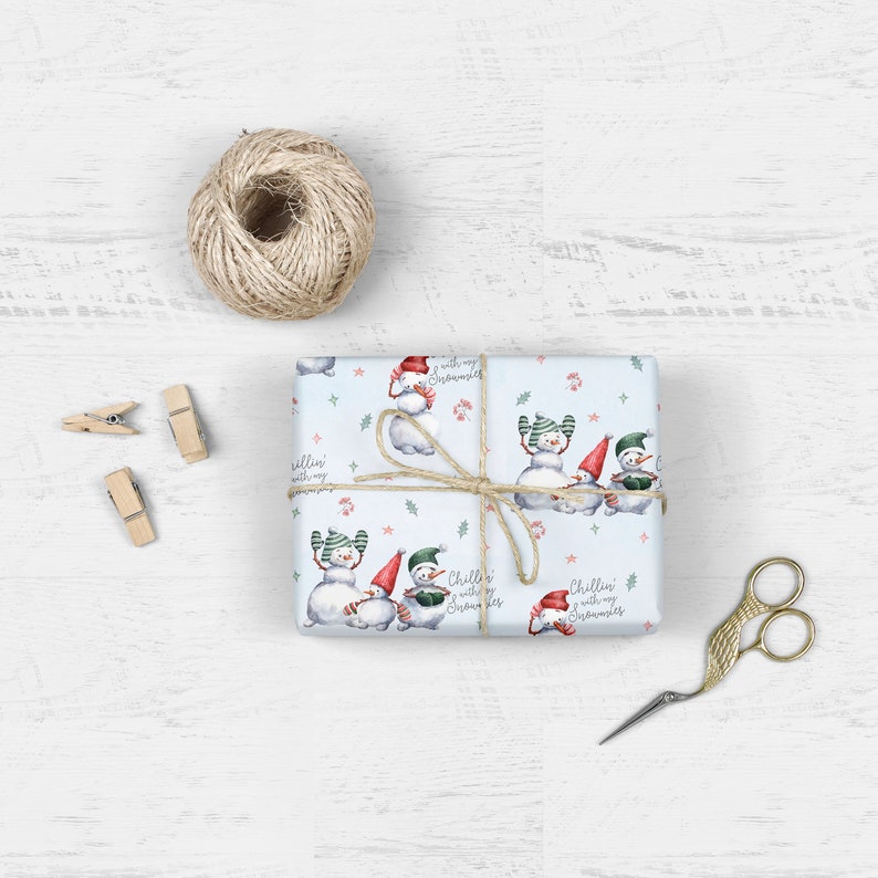 May include: Blue wrapping paper with a repeating pattern of snowmen wearing hats and scarves. The paper has the text "Chillin' with my snowmies" repeated throughout.