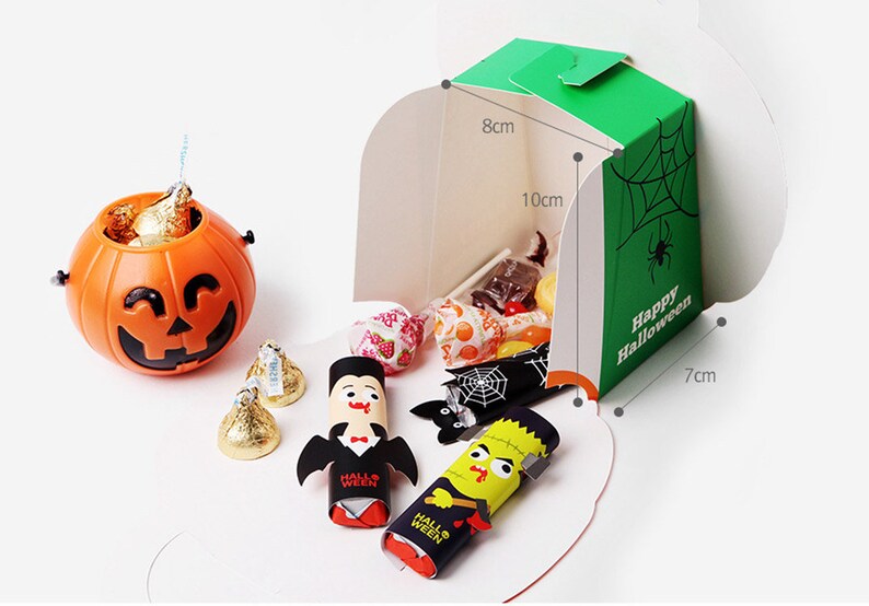 May include: An orange plastic jack-o'-lantern bucket filled with gold-wrapped candies, alongside a green cardboard box labeled Happy Halloween with dimensions 8cm by 10cm by 7cm, containing assorted sweets, a vampire figure, and a monster figure.