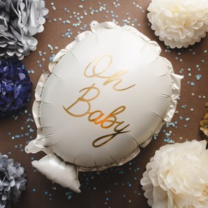 May include: A white balloon with the text "Oh Baby" written in gold script. The balloon is surrounded by white, gold, and blue tissue paper pom-poms.
