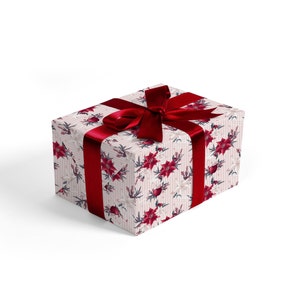 Pode incluir: Uma caixa de presente branca com uma fita vermelha e um padr&atilde;o floral de poins&eacute;tias vermelhas e flores brancas. A caixa est&aacute; embrulhada em papel de Natal festivo.
