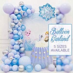 Puede incluir: Una guirnalda de globos azules y morados con estrellas plateadas, un globo de copo de nieve y un pastel tem&aacute;tico de Frozen con una falda de tul azul y estrellas doradas. El texto "Balloon Garland" y "5 Sizes Available" est&aacute; sobre un fondo blanco.