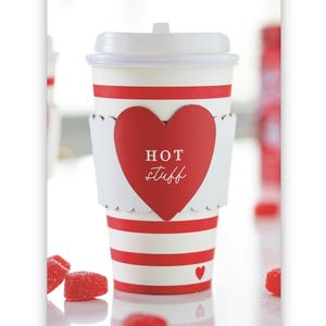 May include: Red and white striped paper cup with a red heart-shaped paper sleeve that says "HOT stuff" in white lettering. The cup is sitting on a white surface with red candy hearts scattered around it.