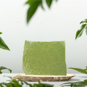 Può includere: Una saponetta verde su un pezzo di legno, circondata da foglie verdi.