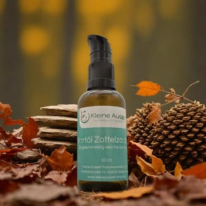 Op de afbeelding: Een flesje van 50 ml Zottelzau baardolie met een groen label waarop "Kleine Auszeit Naturkosmetik" en "Hartöl Zottelzau" in het Duits staat. Het flesje staat op een bed van bruine bladeren en dennenappels.