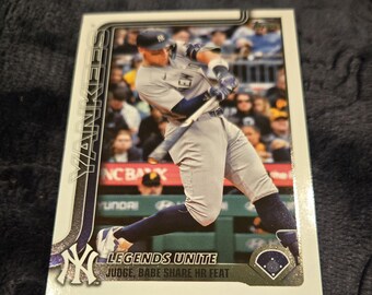 May include: A baseball card featuring a player in a New York Yankees uniform swinging a bat. The card has the text "Yankees" vertically on the left side and "LEGENDS UNITE" at the bottom. The card has a baseball field graphic.