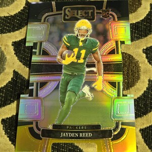 May include: A football trading card featuring Jayden Reed of the Packers. The card has a holographic design with the player in a green and yellow uniform. The card includes the text "Select 2023" and "Packers Jayden Reed".