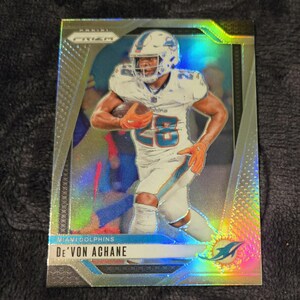 May include: A De'Von Achane Miami Dolphins football trading card. The card features a player in a white and aqua uniform, holding a football. The card has a holographic, iridescent finish with the team logo in the bottom right corner.