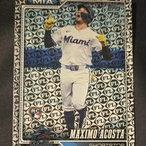 May include: A baseball card featuring Maximo Acosta of the Miami Marlins. The card has a patterned background with the team logo and player's name. Acosta is in a baseball uniform, pointing upwards.