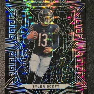 May include: A silver and black football trading card with a holographic finish. The card features a photo of Tyler Scott, a rookie player for the Chicago Bears, wearing a black jersey with the number 13. The card has the words "Obsidian" and "Rookie RC Card" printed on it.