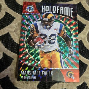 May include: A football trading card featuring Marshall Faulk of the St. Louis Rams. The card has a holographic background with the words "HOLOFAME" at the top. Faulk is wearing a Rams uniform with the number 28.