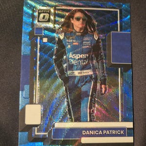 May include: A Danica Patrick Optic trading card. The card features a photo of Danica Patrick in a blue racing suit with the Aspen Dental logo. The card has a blue holographic background and the Optic logo in the upper left corner.