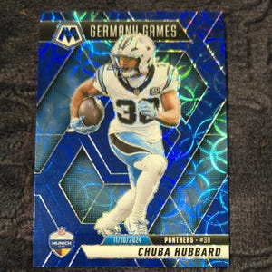 May include: A blue and silver football trading card featuring a player in a Carolina Panthers uniform. The card reads "GERMANY GAMES" at the top and "CHUBA HUBBARD" at the bottom. The date "11/10/2024" is also visible.