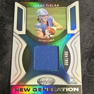 May include: A Detroit Lions football card featuring Isaac Teslaa. The card has a blue jersey swatch and the text "2025 Certified New Generation". The card is numbered 058/499 and has a Rookie Card logo.