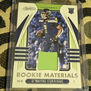 May include: A green and white football card featuring a Seattle Seahawks player, D'Wayne Eskridge, with the text "Rookie Materials" and "WR D'WAYNE ESKRIDGE".