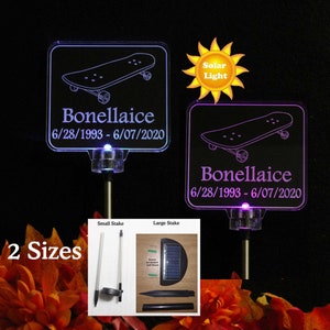 May include: Two sizes of solar-powered memorial lights with a skateboard design. The larger light has a purple glow and the smaller light has a blue glow. Both lights have the text "Bonellaice 6/28/1993 - 6/07/2020" on them.