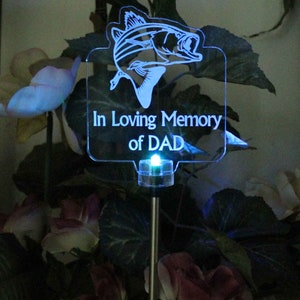 Pode incluir: Uma estaca de jardim solar LED azul com uma placa de acr&iacute;lico transparente que diz "In Loving Memory of DAD" e uma silhueta de um peixe.