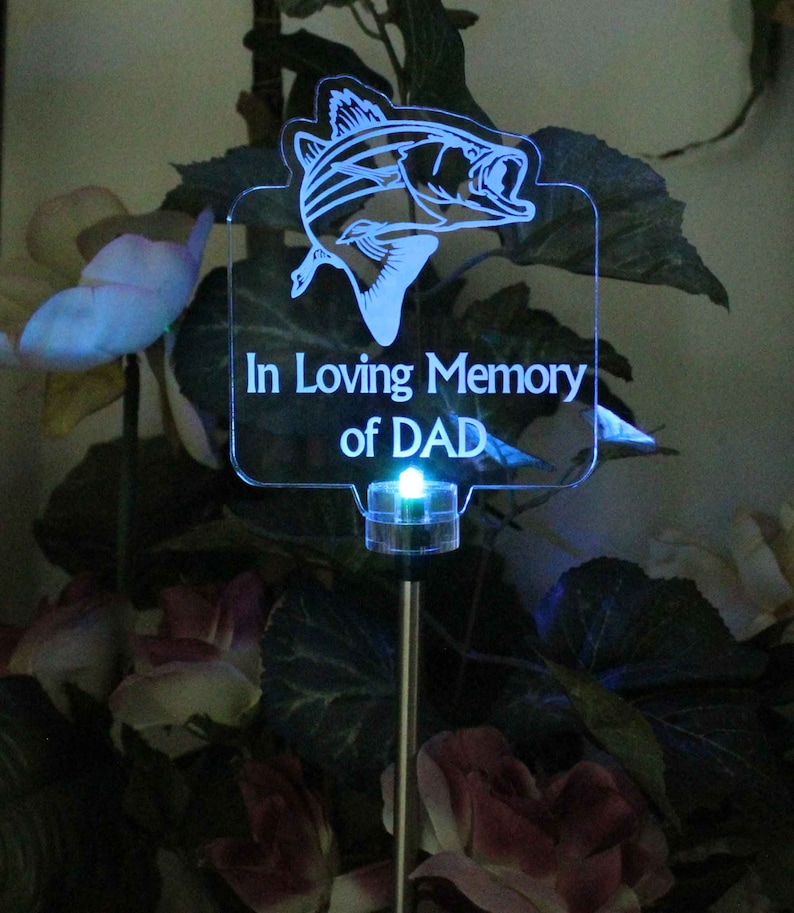 Pode incluir: Uma estaca de jardim solar LED azul com uma placa de acr&iacute;lico transparente que diz "In Loving Memory of DAD" e uma silhueta de um peixe.