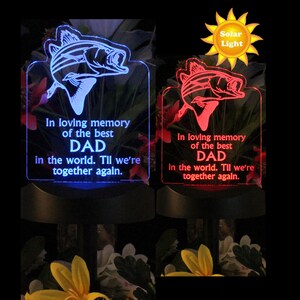 Pode incluir: Uma luz memorial alimentada por energia solar com um visor LED azul e vermelho. A luz apresenta uma silhueta de peixe e o texto "Em mem&oacute;ria carinhosa do melhor PAPAI do mundo. At&eacute; que nos reencontremos."