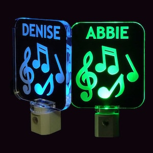 May include: Two square-shaped night lights with personalized names, "DENISE" and "ABBIE", and musical notes. The lights are illuminated in blue and green.