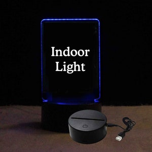 Pode incluir: Uma base de acr&iacute;lico preto com um painel de acr&iacute;lico transparente que acende em azul. O painel tem as palavras "Indoor Light" impressas. A base tem um cabo USB conectado.