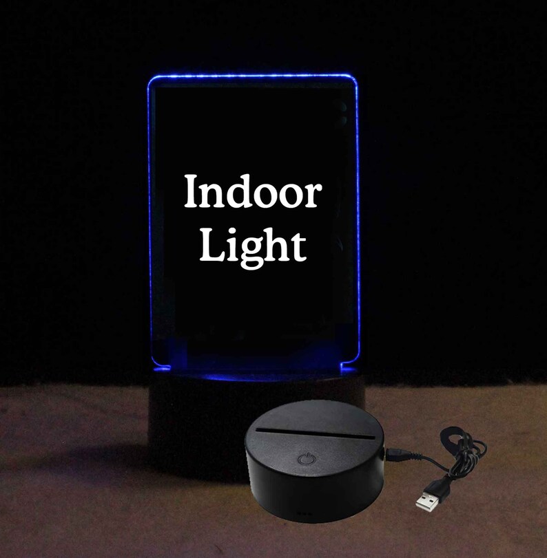 Pode incluir: Uma base de acr&iacute;lico preto com um painel de acr&iacute;lico transparente que acende em azul. O painel tem as palavras "Indoor Light" impressas. A base tem um cabo USB conectado.