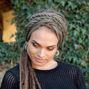Puede incluir: Una persona con largas rastas marrones lleva una diadema trenzada verde oscuro y una camiseta de malla negra. La diadema está anudada en la parte posterior de la cabeza. La persona está mirando hacia abajo.