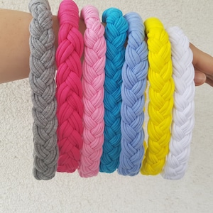 Può includere: Un set di sette fasce per capelli intrecciate in vari colori, tra cui grigio, rosa, rosa chiaro, blu, blu chiaro, giallo e bianco.