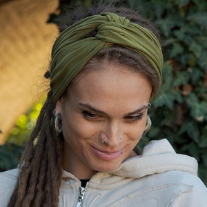 May include: An olive green fabric headband featuring a central twisted knot design. The headband is made of a soft, stretchy material and is worn across the forehead, providing a secure fit while keeping hair pulled back from the face.