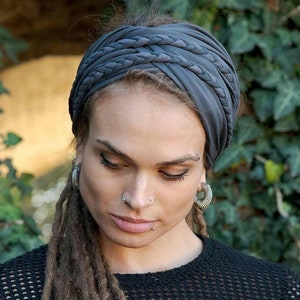 May include: A dark gray fabric headband featuring a wide, gathered design with multiple braided strands across the top. The headband is constructed from a soft, matte material that wraps around the head, creating a layered and textured appearance.