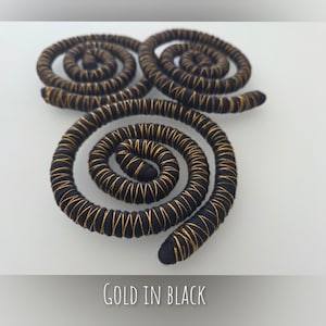 K&ouml;nnte beinhalten: Drei spiralf&ouml;rmige Dekorationselemente aus schwarzer Kordel, die mit d&uuml;nnem goldenem Metallic-Faden umwickelt sind. Die Spiralen sind in einer Dreiecksform angeordnet. Der Text "GOLD IN BLACK" steht in Wei&szlig; am unteren Bildrand.