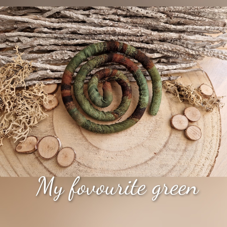 May include: A fabric spiral in shades of green and brown with a textured surface. The spiral is coiled into a circular shape. Below the spiral, the text "My fovourite green" is written in a white cursive font against a light brown background.