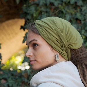 May include: An olive green head wrap made of soft, lightweight fabric. The head covering features a gathered, twisted design at the front and fits snugly around the head, covering the hair completely while leaving the face and ears visible.
