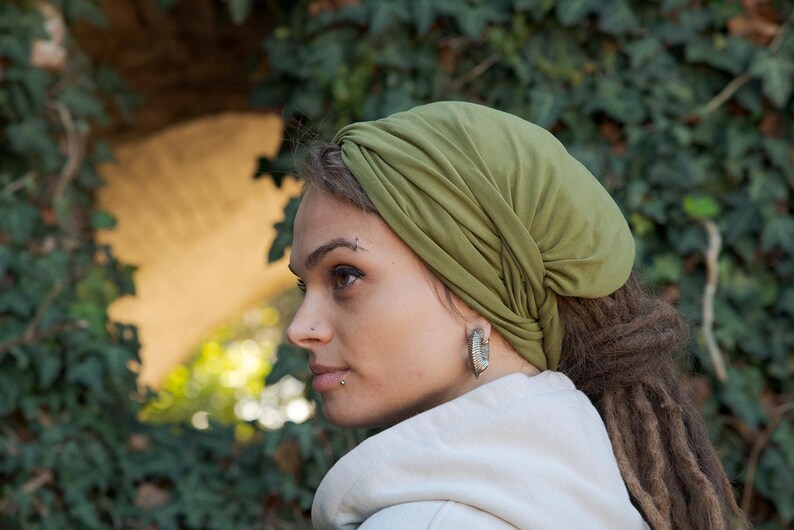 May include: An olive green head wrap made of soft, lightweight fabric. The head covering features a gathered, twisted design at the front and fits snugly around the head, covering the hair completely while leaving the face and ears visible.