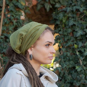 May include: An olive green slouchy beanie hat made of soft fabric, featuring a gathered design that creates a relaxed fit. The hat is worn covering the top of the head, showcasing a solid, muted green color and a smooth, lightweight texture.