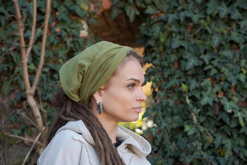 May include: An olive green slouchy beanie hat made of soft fabric, featuring a gathered design that creates a relaxed fit. The hat is worn covering the top of the head, showcasing a solid, muted green color and a smooth, lightweight texture.