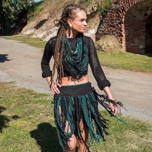 May include: A black mesh long-sleeve crop top, paired with a black and green fringed skirt. The skirt features long, flowing strips of fabric in black and teal. A matching scarf completes the bohemian ensemble.
