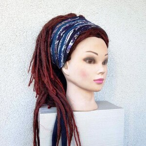 May include: A blue and purple patterned headband with a dark blue tie. The headband is worn on a mannequin with long, red dreadlocks.