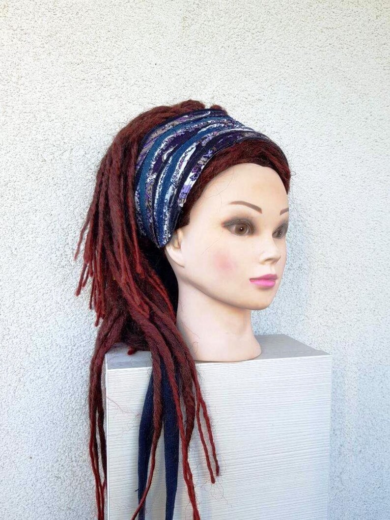 May include: A blue and purple patterned headband with a dark blue tie. The headband is worn on a mannequin with long, red dreadlocks.