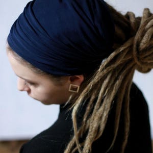 May include: A dark navy blue head wrap made of a smooth, stretchy fabric. The head wrap is styled with multiple horizontal folds and gathers, covering the crown of the head securely while leaving the hair styled in long, light brown dreadlocks.