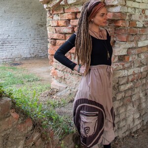 K&ouml;nnte beinhalten: Eine Frau mit langen Dreadlocks tr&auml;gt ein schwarzes Oberteil und einen braunen, mehrlagigen Rock mit einer gro&szlig;en Tasche. Sie steht neben einer Backsteinmauer und tr&auml;gt schwarz-wei&szlig;e Turnschuhe.