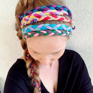 Può includere: Una donna indossa una fascia per capelli realizzata in tessuto intrecciato di vari colori, tra cui rosa, blu, verde, giallo e viola. La fascia è indossata sulla fronte e il tessuto è intrecciato in un motivo semplice.