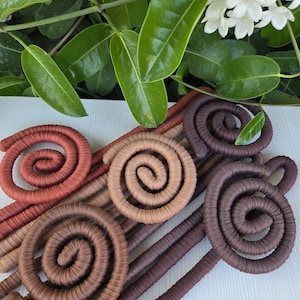 Puede incluir: Una colecci&oacute;n de cinco objetos decorativos en forma de espiral envueltos en tela, con un degradado de tonos tierra que incluye terracota, beige, marr&oacute;n claro, marr&oacute;n medio y marr&oacute;n chocolate oscuro, dispuestos en un patr&oacute;n superpuesto.