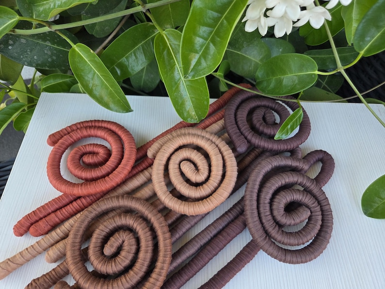 Puede incluir: Una colecci&oacute;n de cinco objetos decorativos en forma de espiral envueltos en tela, con un degradado de tonos tierra que incluye terracota, beige, marr&oacute;n claro, marr&oacute;n medio y marr&oacute;n chocolate oscuro, dispuestos en un patr&oacute;n superpuesto.