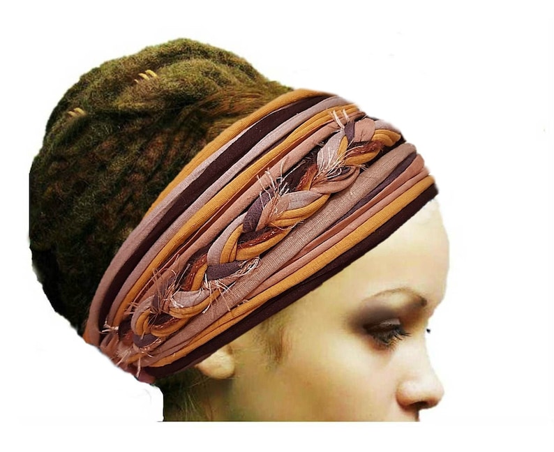 Puede incluir: Una diadema ancha de tela con m&uacute;ltiples tiras horizontales de material de punto en tonos marr&oacute;n, beige y malva. El dise&ntilde;o incluye una secci&oacute;n central trenzada con bordes deshilachados, creando una apariencia texturizada y en capas.