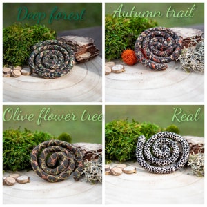 May include: Four spiral-shaped fabric coils displayed in a grid. The top left is dark green with a forest pattern labeled Deep forest. The top right is orange and black labeled Autumn trail. The bottom left is dark with olive flowers labeled Olive flower tree. The bottom right is black and white spotted labeled Real.