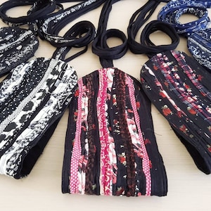 Op de afbeelding: Een verzameling van vijf rechthoekige stoffen tasjes met lange zwarte banden, voorzien van diverse patchworkontwerpen in zwart, wit, roze en blauwe patronen, waaronder bloemen-, stippen- en ruitmotieven, gerangschikt in een waaiervorm.