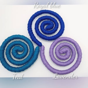 May include: Three spiral-shaped fabric-wrapped coils arranged in a triangular formation. The top coil is royal blue, the bottom left is teal, and the bottom right is lavender. Each coil features a smooth, tightly wound textile texture.