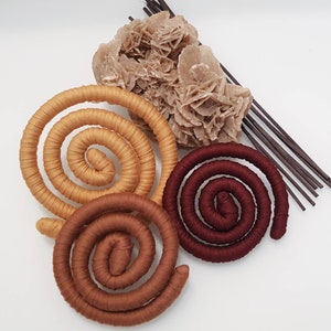 May include: Three coiled, fabric-wrapped circular objects in shades of tan, medium brown, and deep burgundy. Accompanying these are a cluster of light beige, crystalline desert rose mineral formations and a bundle of thin, dark brown wooden sticks.