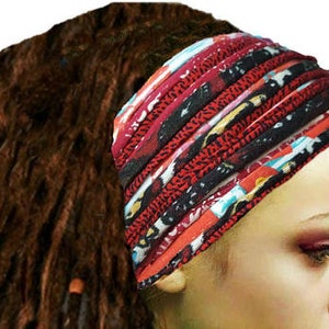 May include: A wide, multi-layered fabric headband featuring a vibrant pattern of red, black, white, and blue colors. The accessory is constructed from several horizontal bands of fabric that create a gathered, textured appearance across the forehead.