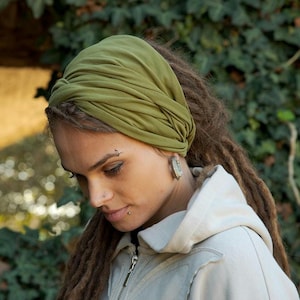 May include: An olive green fabric headband featuring a twisted knot design at the front. The headband is made of a soft, stretchy material that wraps around the head, creating a gathered, layered appearance with visible folds in the fabric.